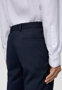 Pantaloni blu navy con una texture liscia e un taglio slim, abbinati a una camicia bianca con bottoni ai polsini e un design su misura.