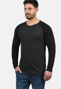 Schwarzes Langarm-T-Shirt mit einem dunkelgrauen Körper, kontrastierenden schwarzen Raglanärmeln, aus weichem Stoff. Hat einen Rundhalsausschnitt und eine lockere Passform.