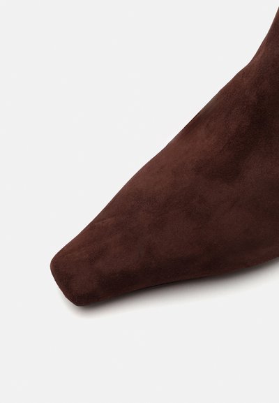 Brązowy zamszowy but na szpilce o gładkiej strukturze i minimalistycznym designie. But ma zwężoną sylwetkę.