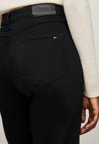 Mustad teksad kõrge vöökohtadega, millel on taga nahkne Tommy Hilfiger silt ja taskul väike lipu aktsent.