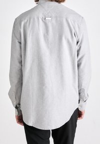 Uomo che indossa una camicia a maniche lunghe grigia chiaro con polsini abbottonati, visto da dietro, abbinata a pantaloni neri.