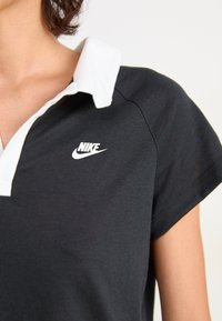 Čierne polo tričko s bielym golierom a krátkymi rukávmi. Obsahuje biele logo Nike na hrudi, vyrobené z priedušného bavlneného materiálu.