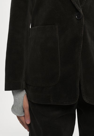 Black corduroy blazer with vertical ribbing, single button closure, and patch pocket. Sleeve features gray knit inset. Textured fabric.
