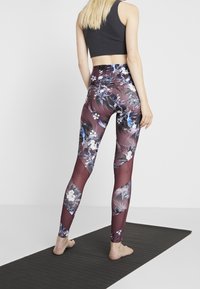 Leggings med ett blommönster i vinröd och blått, med genomskinliga paneler, kombinerade med en svart crop top. Slät, elastisk tyg.