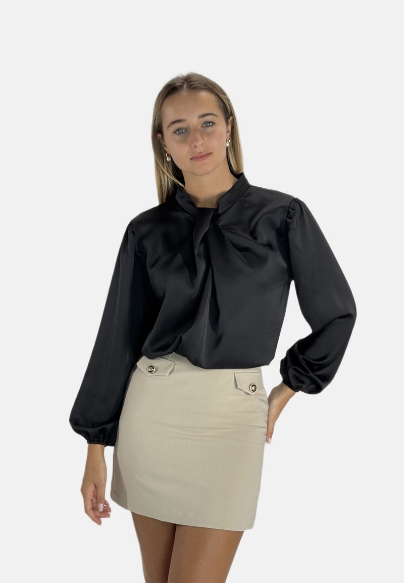 Blusa nera in satin con maniche a sbuffo e scollatura annodata, abbinata a una minigonna beige con due tasche frontali e dettagli in oro.
