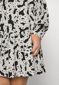 Vestido negro con un patrón de cadenas blancas, con falda plisada y mangas largas y abullonadas. La tela parece suave y liviana.