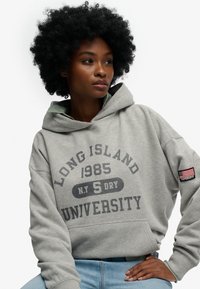 Grå hættetrøje med forlomme, med teksten "LONG ISLAND 1985 N.Y. S DRY UNIVERSITY" trykt på fronten. Indeholder et "SUPERDRY" mærkat med et amerikansk flag.