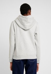 Sudadera gris claro con una gran capucha de doble capa, puños y dobladillo acanalados. La tela tiene una textura suave y un ajuste relajado.