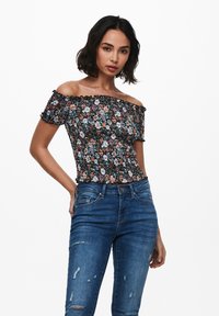 Kvetinový off-shoulder top s čiernym pozadím, volánovými okrajmi a smockovaným dizajnom. Nosený s roztrhnutými modrými džínami.