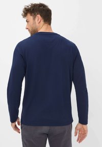 Marineblauw long-sleeve shirt van zacht materiaal, met een ronde hals en minimale stikdetails, gecombineerd met grijze broeken.