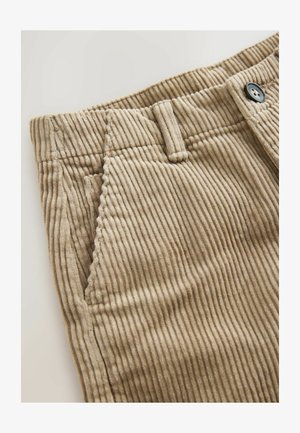 Barna kordbársony nadrág függőleges bordázással, oldalzsebbel és fekete gombbal. A sima textúra jól illeszkedik a szabott dizájnhoz.