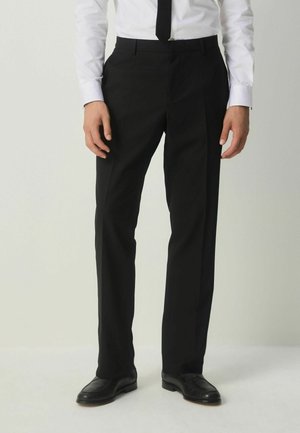 Pantalones negros de corte entallado con un diseño de pierna recta, hechos de un tejido suave. Presentan una parte delantera plana y trabillas para cinturón, combinados con zapatos de vestir negros.