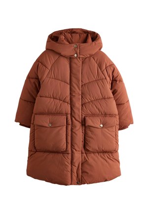 Junges Mädchen steht mit den Händen in den Taschen, trägt einen langen rostfarbenen Steppmantel mit Kapuze, beige weite Hosen und weiße Sneaker.