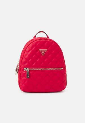 Mini sac à dos matelassé rouge avec poche avant zippée et logo triangulaire Guess sur fond blanc.