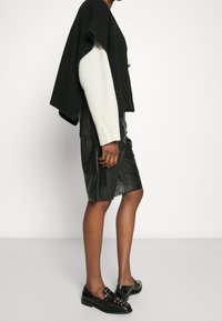 Czarny i kremowy sweter dziany z długimi białymi ściągaczami, w zestawie z czarną skórzaną spódnicą z bocznymi kieszeniami oraz płaskimi czarnymi butami.