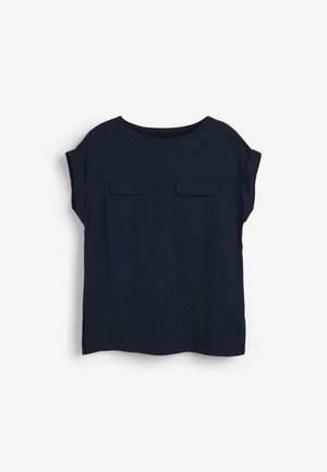 Blouse bleu marine à manches courtes avec encolure arrondie, deux poches à rabat sur la poitrine et petites fentes latérales sur fond blanc.