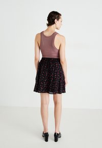 Top sem mangas em tom mauve combinado com uma saia skater preta com padrão floral. A saia apresenta pequenas flores vermelhas e brancas, com uma textura de tecido suave.