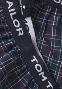 Navy boxer briefs featuring a white, elastic waistband with "TOM TAILOR" branding and a checked pattern in red and light blue.