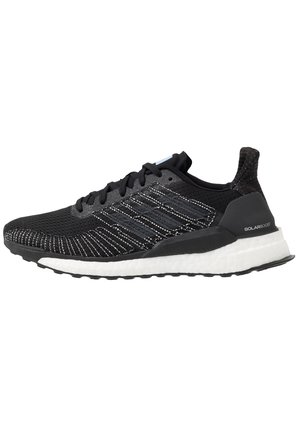 Černá sportovní bota s prodyšným síťovinovým svrškem, bílou texturovanou podrážkou a reflexními akcenty. Disponuje elegantním designem s výrazným šněrováním.