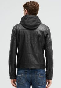 Schwarze Lederjacke mit strukturierter Oberfläche, ausgestattet mit einer Kapuze und taillierter Passform; kombiniert mit blauen Jeans aus Denim mit aufwendigen Nähten.