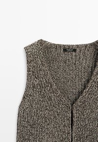 Gilet sans manches tricoté en fil noir et blanc avec col en V et fermeture par boutons, étiquette Massimo Dutti fabriqué en Espagne.
