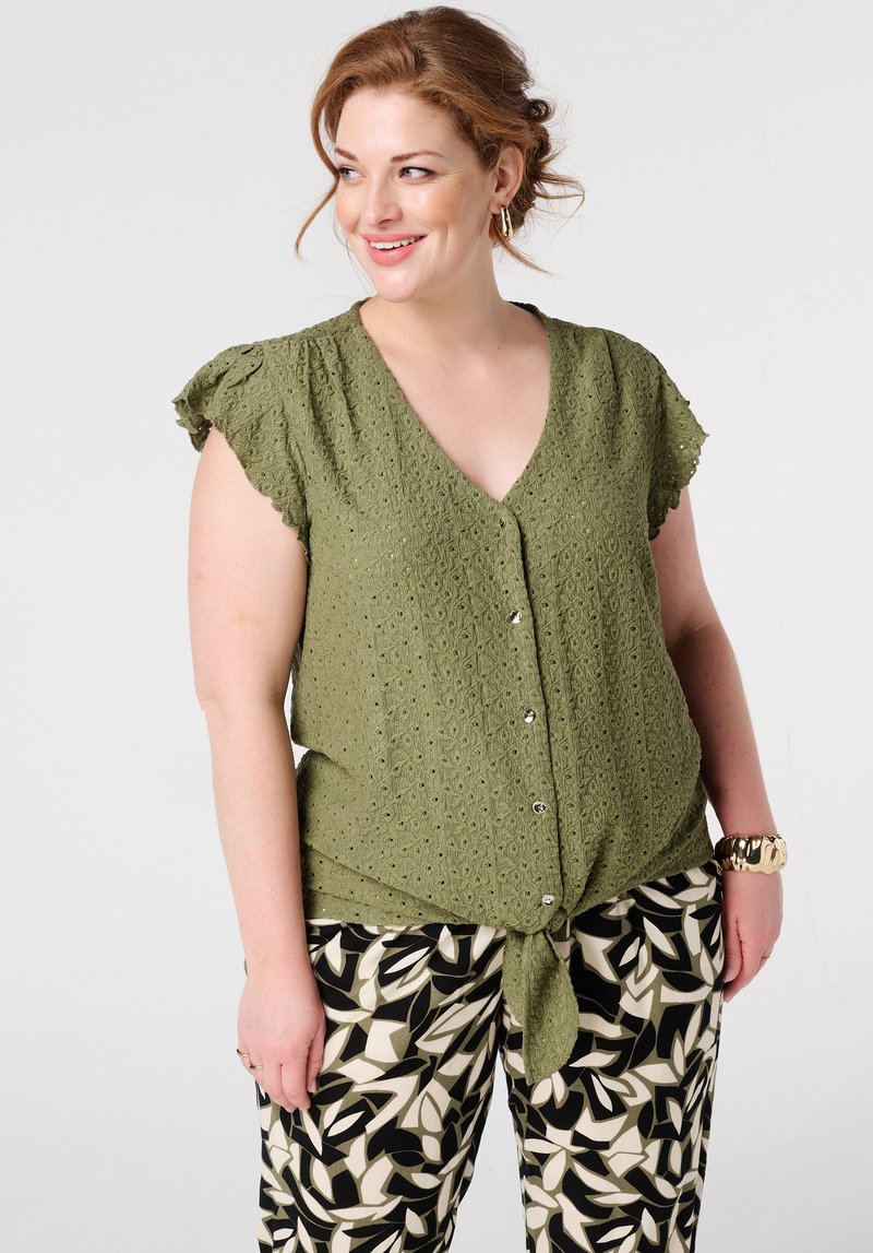 Blouse vert olive à manches courtes avec un col en V, motif texturé et fermeture à boutons. Assorti à un pantalon noir et crème à motifs.