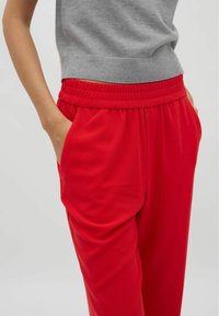 Röda joggers med elastisk midja, sidofickor och en mjuk textur. I kombination med en grå, figurnära stickad topp.