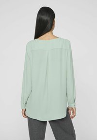 Blusa a maniche lunghe in verde menta chiaro, realizzata in un tessuto morbido. Presenta un collo rotondo sul retro e un leggero orlo a goccia.