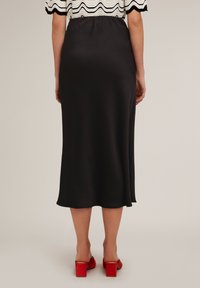 Fustă midi din satin negru, cu o siluetă fluidă, caracterizată printr-o textură netedă și un tiv elastic. Asortată cu pantofi cu toc pătrat roșii.