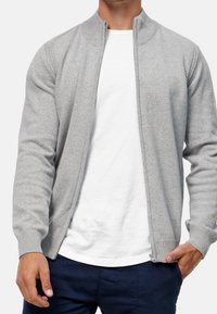 Grå cardigan med lynlås, ribstrikket krave og manchetter. Fremstillet af blødt stof med et rent, strømlinet design og sidelommer.