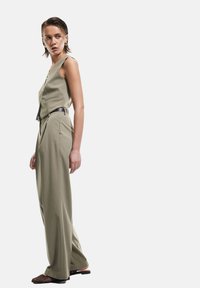 Licht olijfgroen jumpsuit met een aansluitende bodice, wijde pijpen en een zwarte riem. Getextureerde stof met een minimalistisch ontwerp en geen zichtbare patronen.