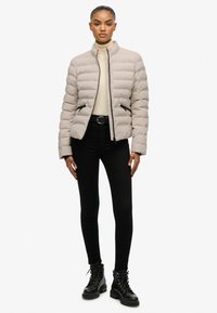 Lichtgrijze donzen jas met een hoge kraag, ritssluiting en zwarte accenten. Gecombineerd met zwarte skinny jeans en zwarte combatlaarzen.