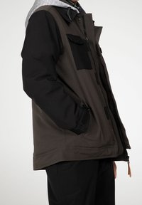 Giacca da uomo con un design a blocchi di colore nero e grigio scuro, dotata di cappuccio grigio, chiusura con zip, tasche frontali e una texture di tessuto morbida.