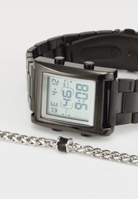 Montre numérique avec un boîtier rectangulaire noir et un bracelet en métal. Affiche un fond blanc et un affichage LED bleu avec plusieurs fonctions.