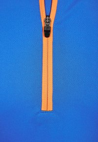 Zip-up topp i klarblått tyg med en orange dragkedja och kontrasterande sömmar. Slät textur, lättviktig, lämplig för aktiv klädsel.