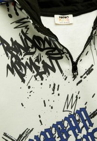 Børns zip-up hættetrøje med en sort hætte og hvid krop, der prydes af abstrakte grafitter med sort og blå grafik. Fremstillet af blødt stof.