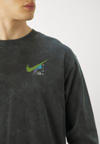 Black cotton sweatshirt featuring a green Nike logo and a graphic design with blue and purple accents on a textured surface.