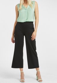 Blusa sin mangas en menta con escote en forma de V; combinada con pantalones de pierna ancha de talle alto en negro; acentuada con tacones de tiras en verde claro.