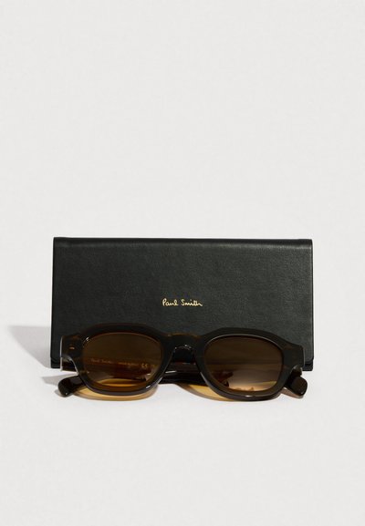 Gafas de sol con lentes tintadas en marrón y montura gruesa de carey, acompañadas de un estuche de cuero negro con el logo "Paul Smith" en relieve.