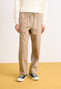 Bežové bavlnené jogger nohavice s elastickým pásom a šnúrkou. Skombinované s čiernymi plátenými teniskami s bielou gumovou podrážkou.