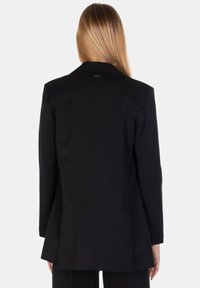 Blazer nero su misura realizzato in tessuto liscio. Presenta un colletto a punta, spalle strutturate e uno spacco singolo sul retro per una maggiore mobilità.