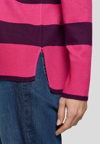 Rosa und dunkelviolett gestreifter Strickpullover mit gerippter Textur, seitlichem Schlitzdetail und langen Ärmeln, kombiniert mit dunkelblauen Jeans.