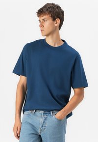 Donkerblauwe t-shirt met een ronde hals en korte mouwen, gemaakt van gladde stof, gecombineerd met lichtblauwe denim jeans.
