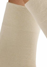 Helle beige Kompressionsstrümpfe mit einem strukturierten oberen Bund und glattem Körper, ausgestattet mit einem gerippten Strickmuster und elastischem Material für Unterstützung.