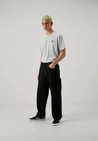 Gray cotton t-shirt with a small black logo, paired with loose-fitting black denim jeans. Footwear features black and white sneakers.