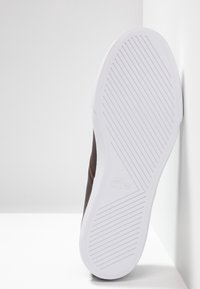 Baskets marron avec une tige en cuir lisse, une semelle extérieure en caoutchouc blanc dotée d'un motif de grip texturé et un discret accent de logo.