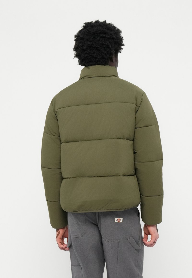 Olivgrüner Pufferjacke mit horizontalen Nähten und hohem Kragen, aus glattem Stoff gefertigt. Zu den Details gehört ein Etikett im unteren Rückenbereich.