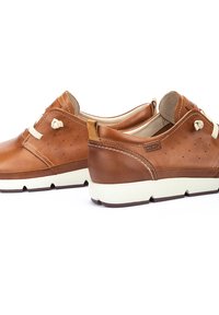 Scarpe di pelle marrone con suole crema, caratterizzate da una finitura liscia, chiusura con lacci, piccole perforazioni sui lati e cuciture a contrasto.