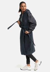 Dark gray long coat with a hood, long sleeves, and a belt. Paired with black skinny jeans and white sneakers with black accents.