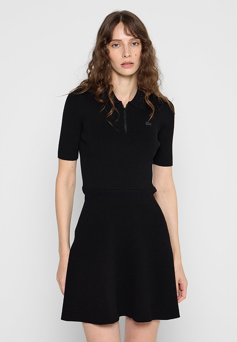 Robe polo noire à côtes avec col zippé, manches courtes, corsage ajusté et jupe évasée. Texture lisse et détails de marque minimalistes.